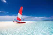 Sailing Boat With Red Sail On A Beach Of Deserted Tropical Islan