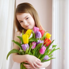 Wall Mural - Adorable little girl holding tulips by the window