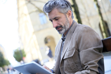 Canvas Print - Mature man websurfing with tablet, sitting on public bench