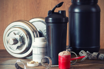 Whey protein powder in scoop with vitamins and plastic shaker