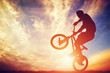 Man riding a bmx bike performing a trick against sunset sky