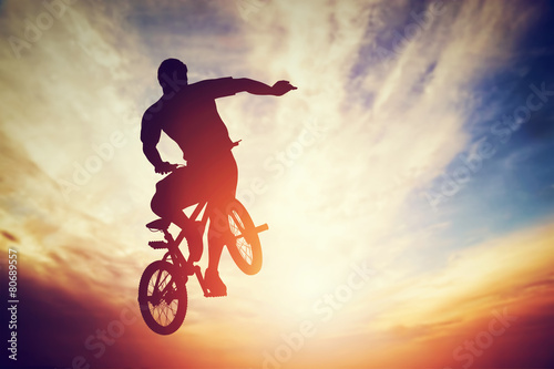 Fényképezés Man jumping on bmx bike performing a trick against sunset sky