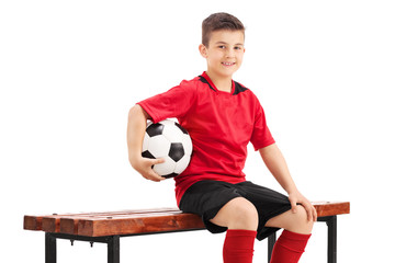 Wall Mural - Junior football player posing seated on a bench