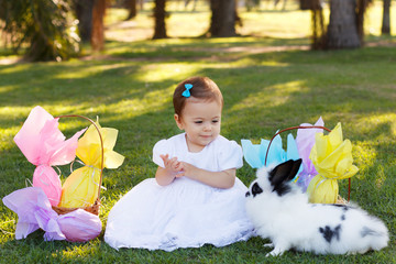 Smiling baby girl looking at rabbit with Easter chocolate eggs