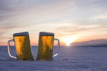 Two mugs of cold beer at sunset