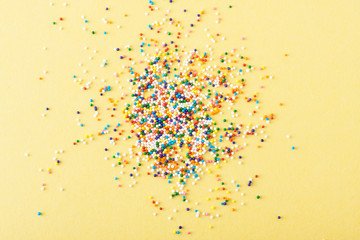 Wall Mural - Colorful round sprinkles spilled on yellow background, isolated