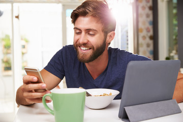 Man Eating Breakfast Whilst Using Digital Tablet And Phone