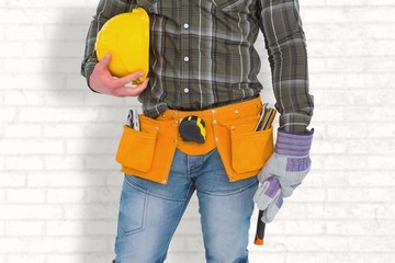 Manual worker wearing tool belt while holding hammer and helmet