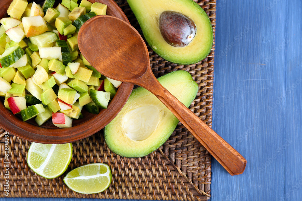 Salad with apple and avocado in bowl on wicker stand close up
