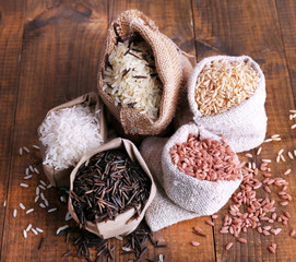 Different types of rice in sacks on wooden background