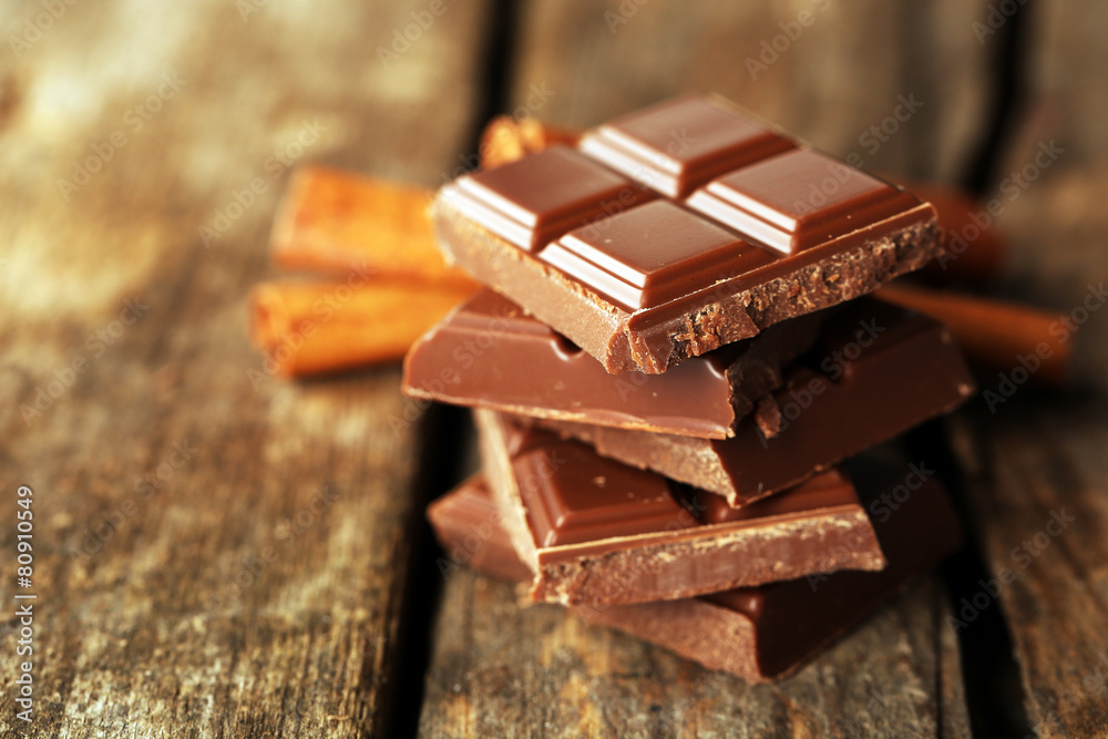 Pieces of chocolate with cinnamon sticks on wooden background