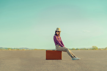 Poster - Traveler girl sitting on suitcase on road in summer