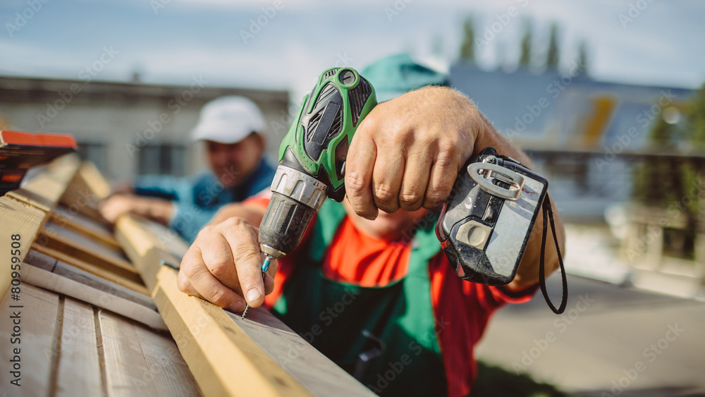 roofer using a drill is fastening a cap to a house roof - obrazy, fototapety, plakaty 