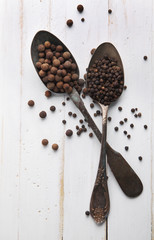 Image of spoons full of black peppercorn and allspice on wooden