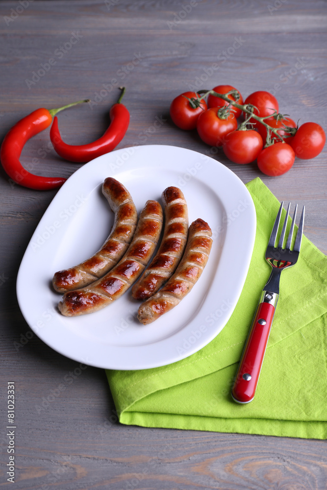 Grilled sausages on plate with vegetables on table close up
