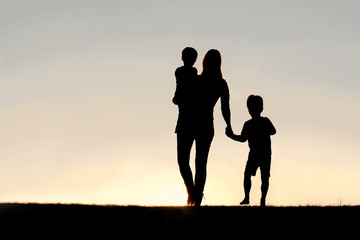 silhouette of walking mother and young children holding hands at