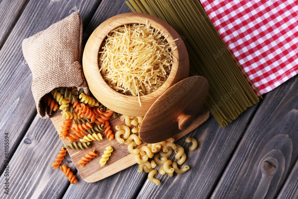 Different types of pasta in containers on wooden background