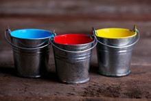 Metal Buckets With Colorful Paint On Wooden Background