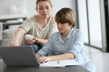 Wall Mural - Mother looking after son doing homework on laptop
