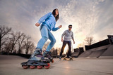 Girl on rollerblades and boy on skateboard in skate park