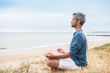 An Attractive Man Is Sitting Face To The Ocean In Lotus Position