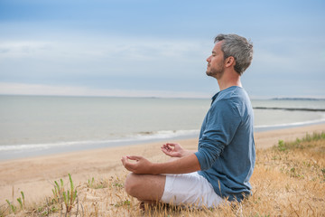 An attractive man is sitting face to the ocean in lotus position