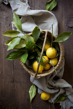 Fresh Lemons With Leaves On Straw Basket On Wooden Table