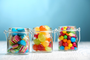 Sticker - Colorful candies in jars on table on blue background background