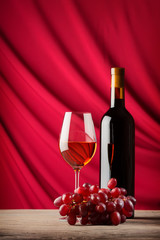 Wall Mural - Bottle and glass of red wine on a background of scarlet satin