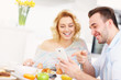 © Kalim - Happy couple eating breakfast and using smart phone