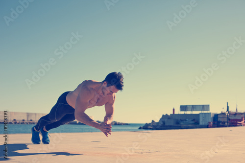 Fotografía Muscular athlete doing jumping push-ups outdoors (intentional vi