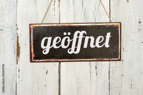 Fotografia Altes Blechschild vor weißer Holzwand - geöffnet