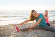 Healthy Mother And Baby Girl Stretching On Beach In The Evening
