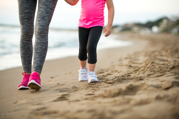 Healthy mother and baby girl walking on beach in the evening