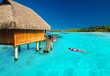 Young woman swimming in tropical lagoon next to overwater villa