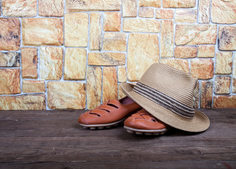 Straw hat and moccasins on a wooden table in front of a stone wa