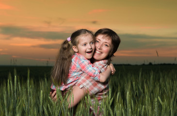 happy mother and child in green field at sunset