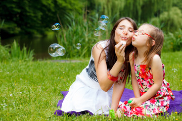 Wall Mural - Mother and little girl blowing soap bubbles in park.