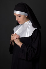 portrait of young woman nun praying with rosary over grey