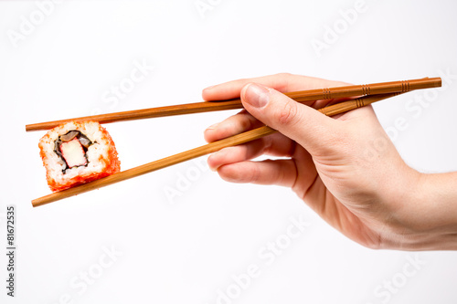 Fotografie, Obraz Hand holding Sushi roll with bamboo chopsticks isolated on white