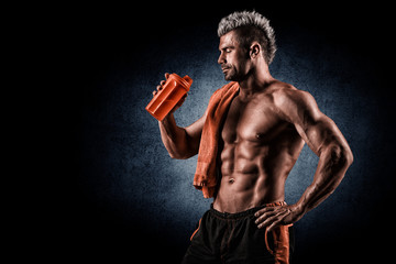 Wall Mural - Young adult man drinking protein shake in gym. Black background.