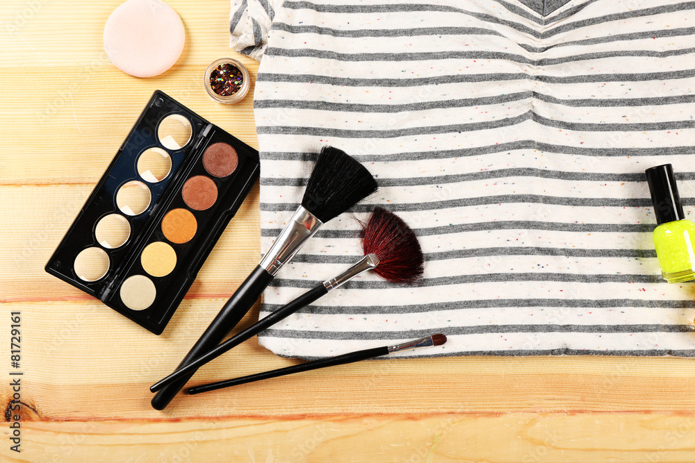 Female shirt and cosmetics on wooden table, top view