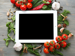 Digital tablet with fresh herbs, tomatoes and spices