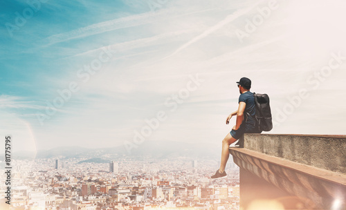 Fotografía Young man is sitting on a roof and looking at the city