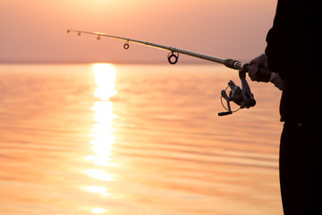 Wall Mural - young girl fishing at sunset near the sea