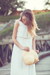 Beautiful young woman in an elegant white dress with a hat in he