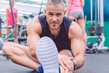 Man stretching and woman doing dumbbells exercises in gym