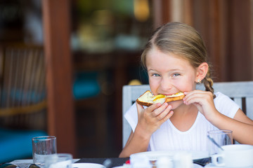 Little adorable girl eating bread with butter and honey on