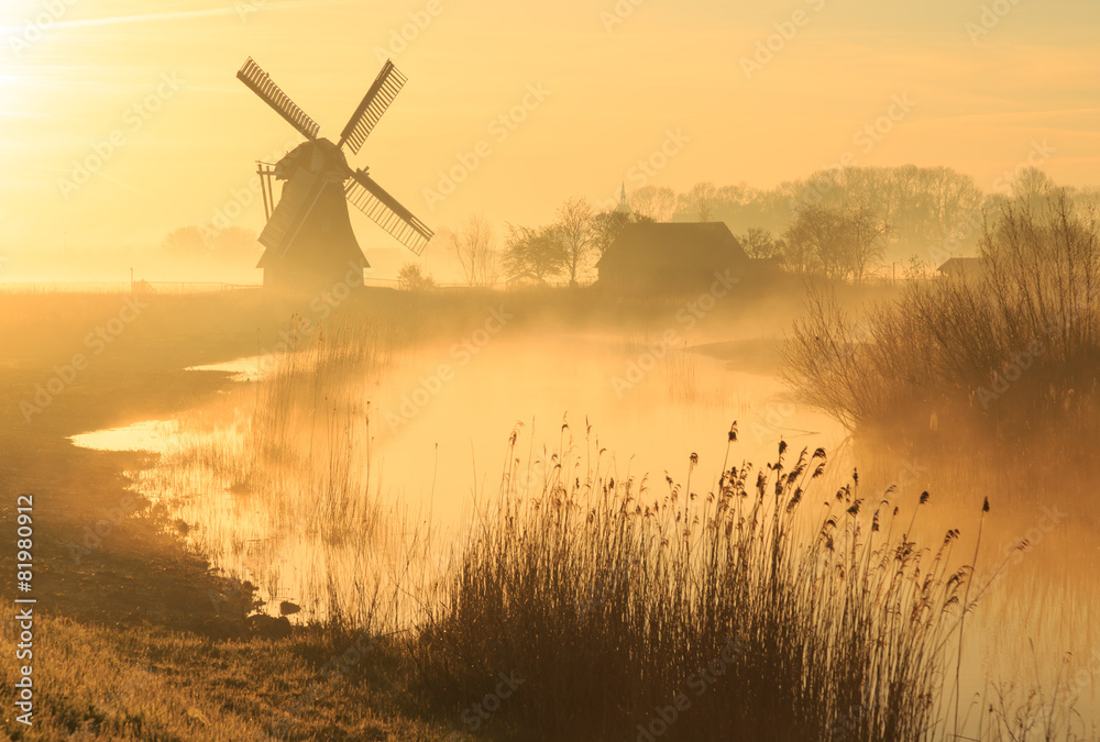 Windmill during a foggy, yellow sunrise in the countryside. - obrazy, fototapety, plakaty 