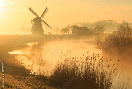 Fotografija Windmill during a foggy, yellow sunrise in the countryside.